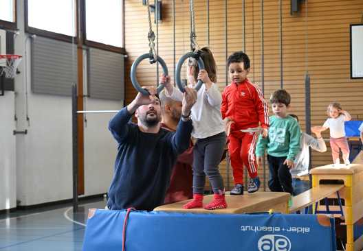 Ein Erwachsener mit Kindern in einer Turnhalle an den Ringen.