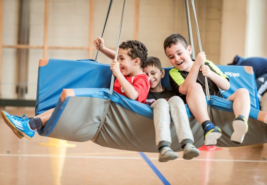 Drei Kinder spielen auf einer an Seilen befestigten Turnmatte